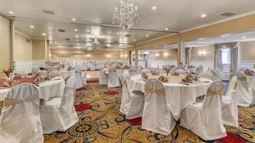 Un salón de banquetes con mesas redondas, manteles blancos y sillas con cintas color beige.
