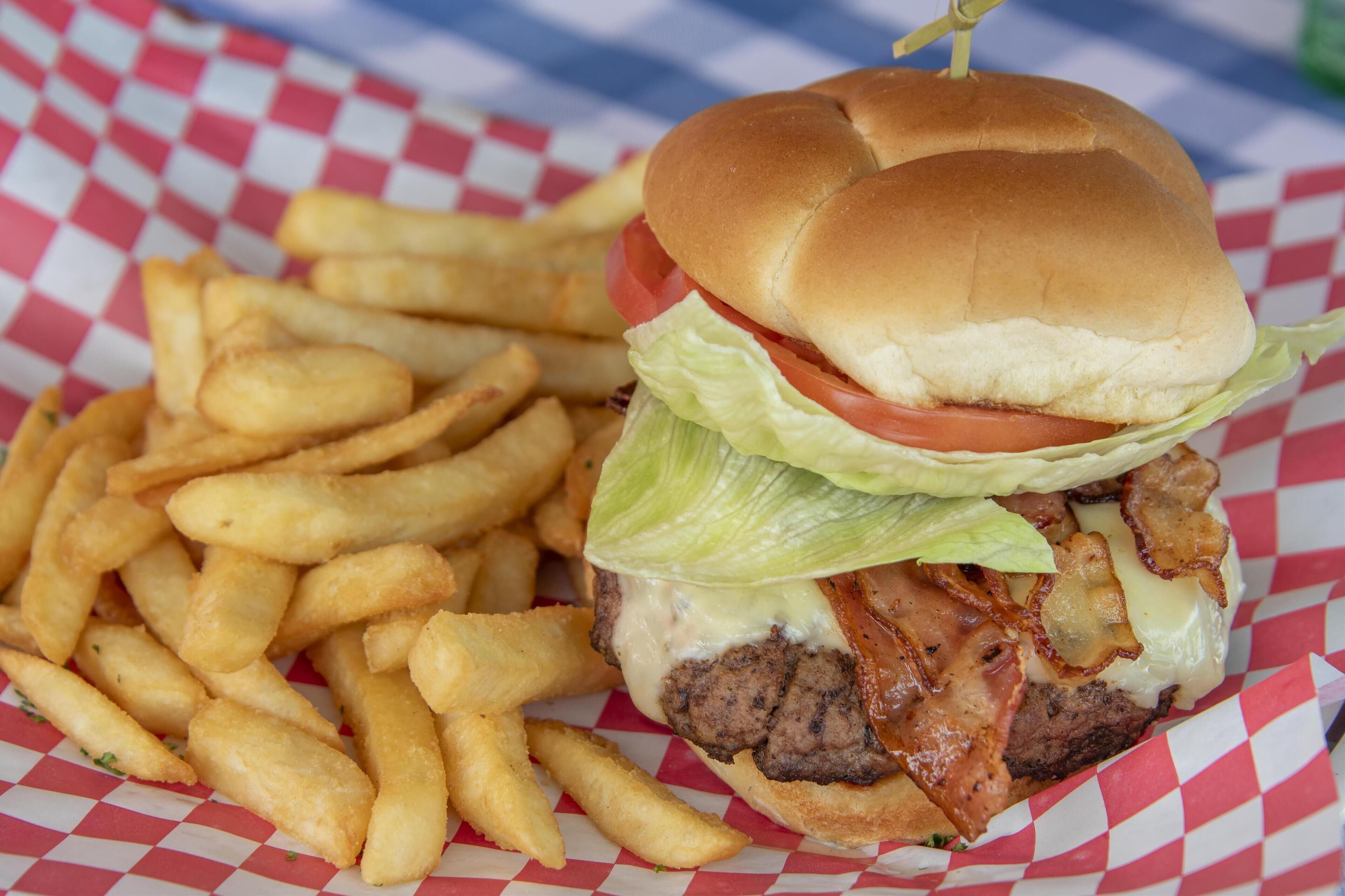 Hamburguesa con lechuga, tomate y tocino, acompañada de una porción de papas fritas sobre un papel cuadriculado.