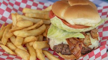 Hamburguesa con lechuga, tomate y tocino, acompañada de una porción de papas fritas sobre un papel cuadriculado.