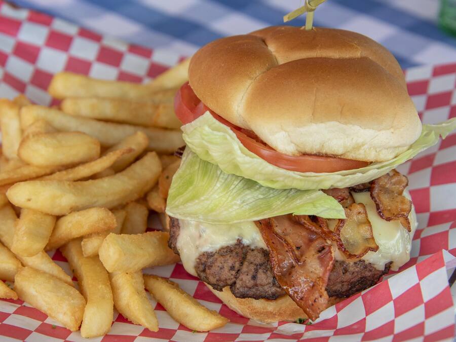 Hamburguesa con lechuga, tomate y tocino, acompañada de una porción de papas fritas sobre un papel cuadriculado.