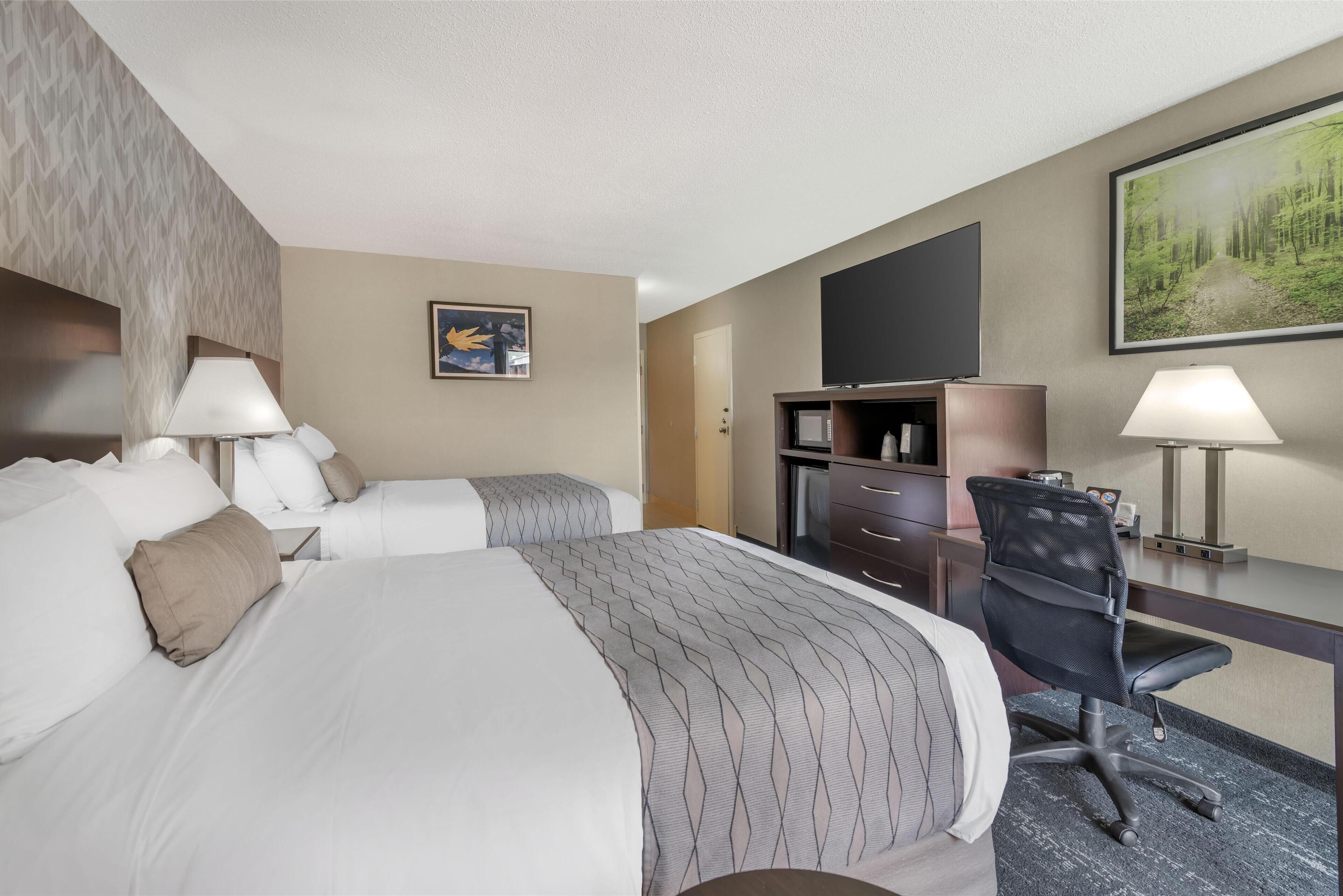 A hotel room with a large bed, two bedside tables, a desk with a chair, a flat-screen TV, and a painting on the wall.