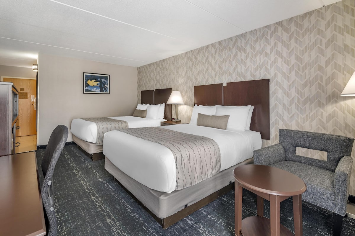 A hotel room with two beds, a desk, a chair, and a small table.