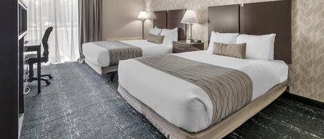 A hotel room with two beds, a desk, and a TV.