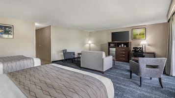 Habitación de hotel con una cama grande, dos sillones, un escritorio con lámpara, un televisor y un pequeño armario.