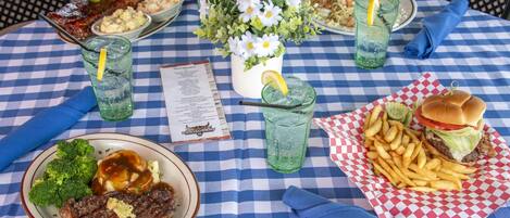 A table set with various dishes including a burger, fries, and a steak with gravy, along with drinks and a menu.