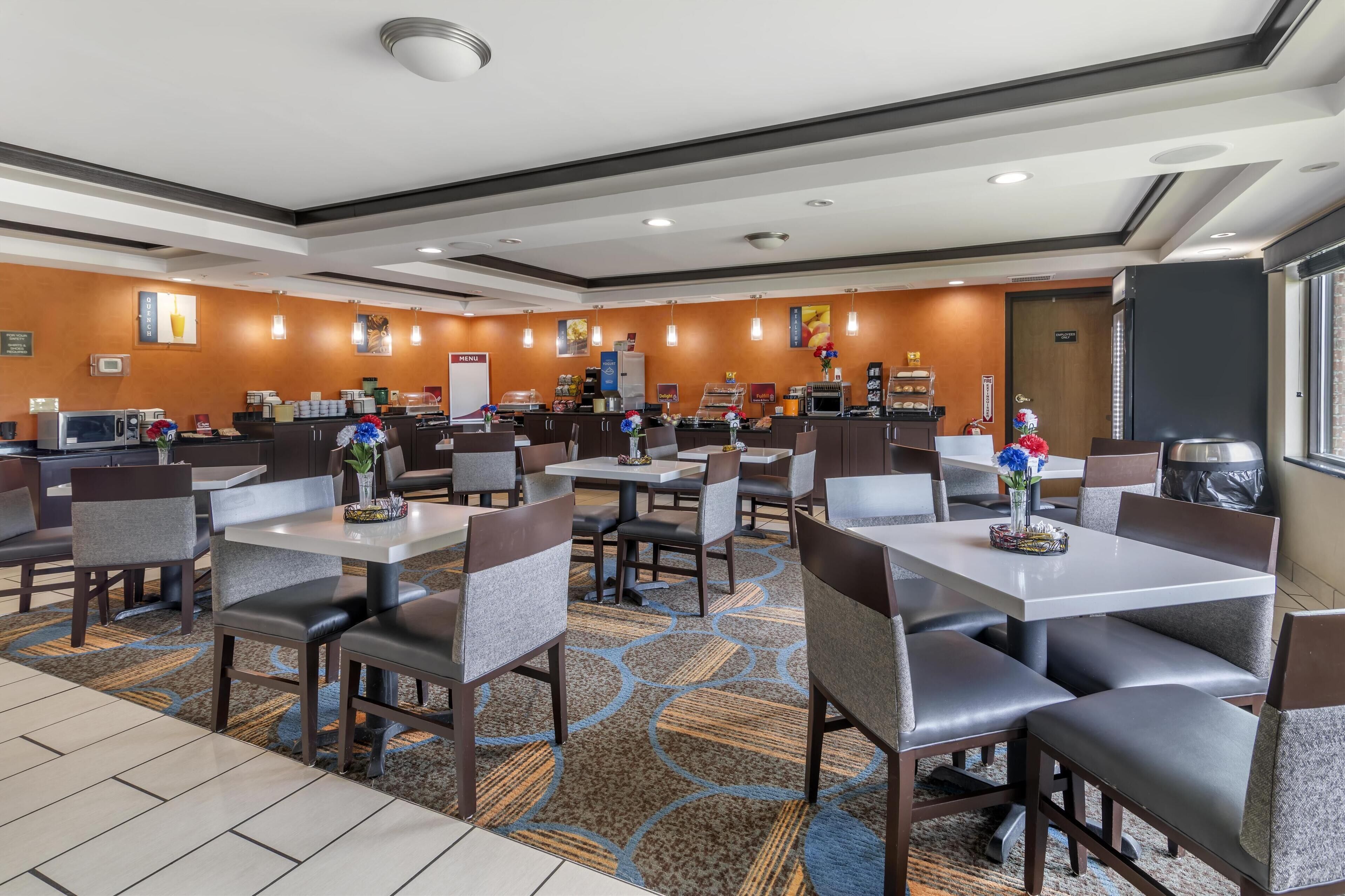 A hotel dining area with multiple tables and chairs, a coffee station, and a kitchen in the background.