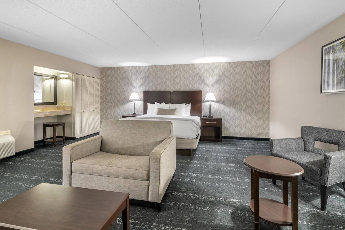 A hotel room with a bed, two bedside tables with lamps, a sofa, a chair, and a small table.