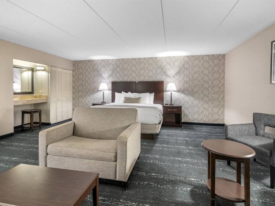 A hotel room with a bed, two bedside tables with lamps, a sofa, a chair, and a small table.