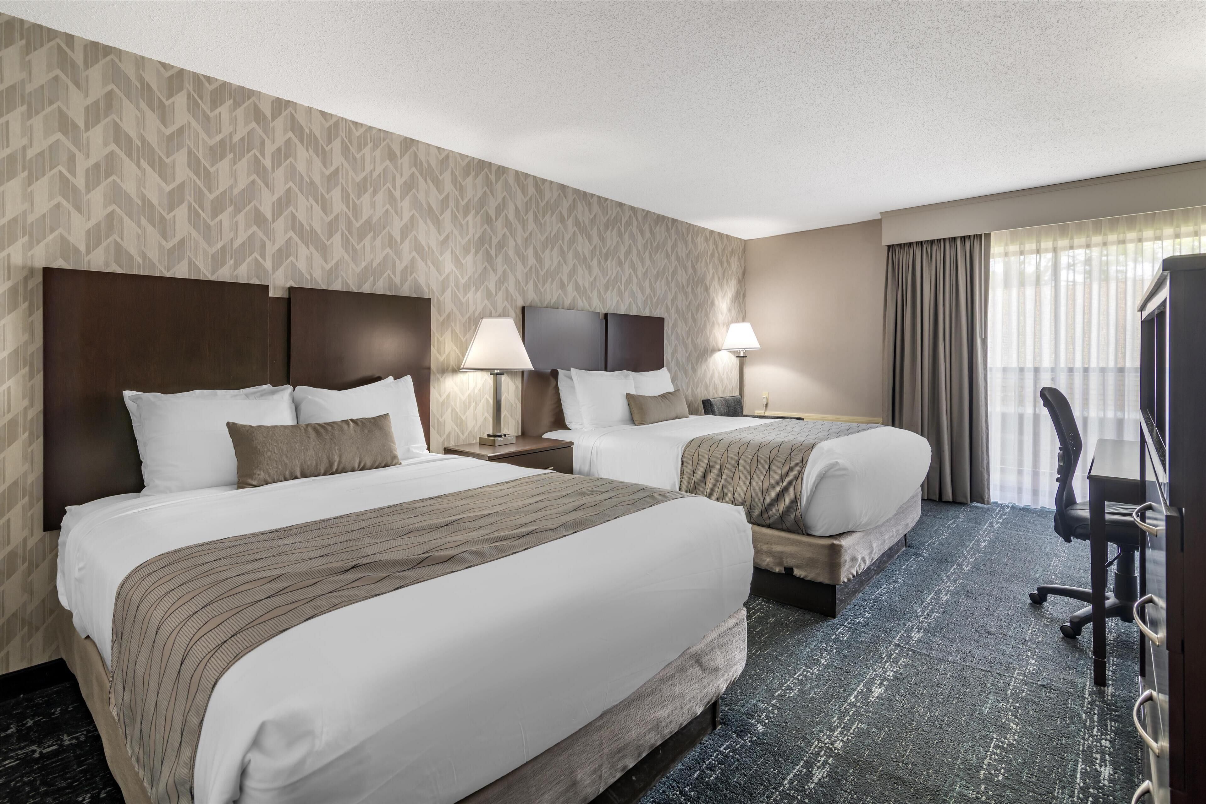 A hotel room with two beds, a desk, and a TV.