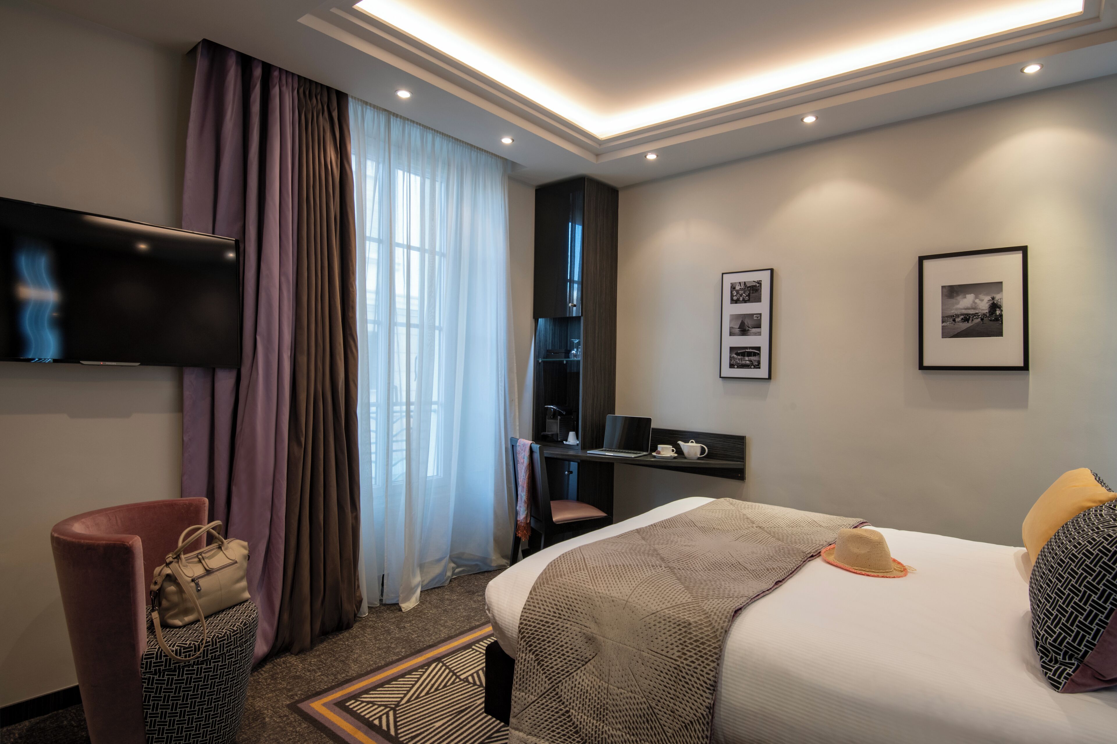 A hotel room with a bed, a desk, a TV, and a chair.