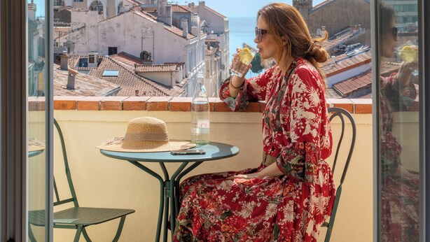 A woman sitting at a table with a view of buildings and the sea. - BW Premier Collection Mondial (Cannes)