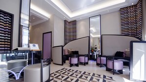 A modern hotel lobby with a geometric patterned floor, a reception desk, seating area with cushioned chairs, and large mirrors. - BW Premier Collection Mondial (Cannes)
