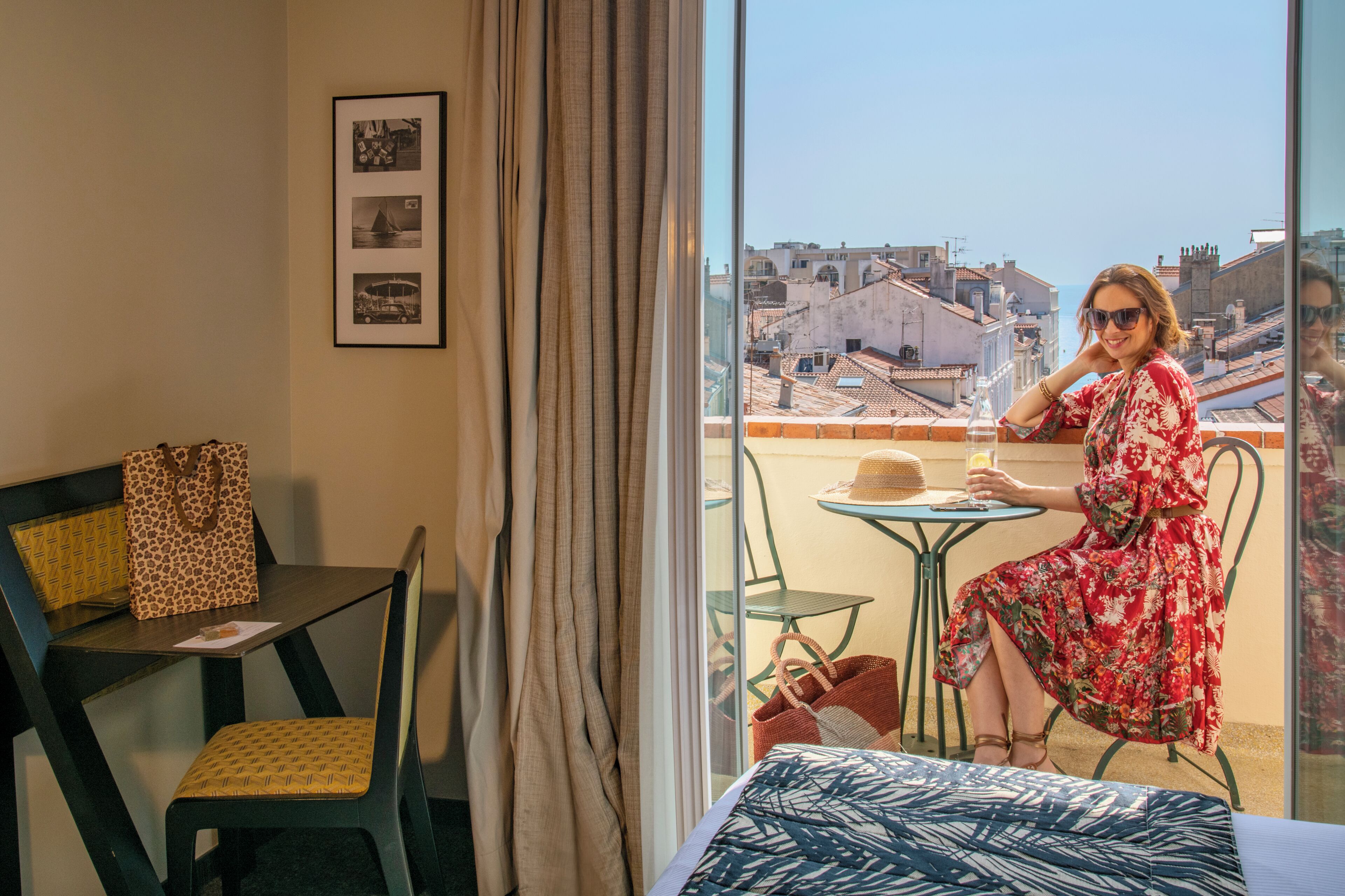 A room with a bed, a chair, a table, and a view of the cityscape through a window.