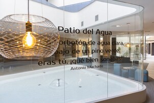 Un área de piscina interior moderna con paredes de vidrio transparente y una lámpara colgante.