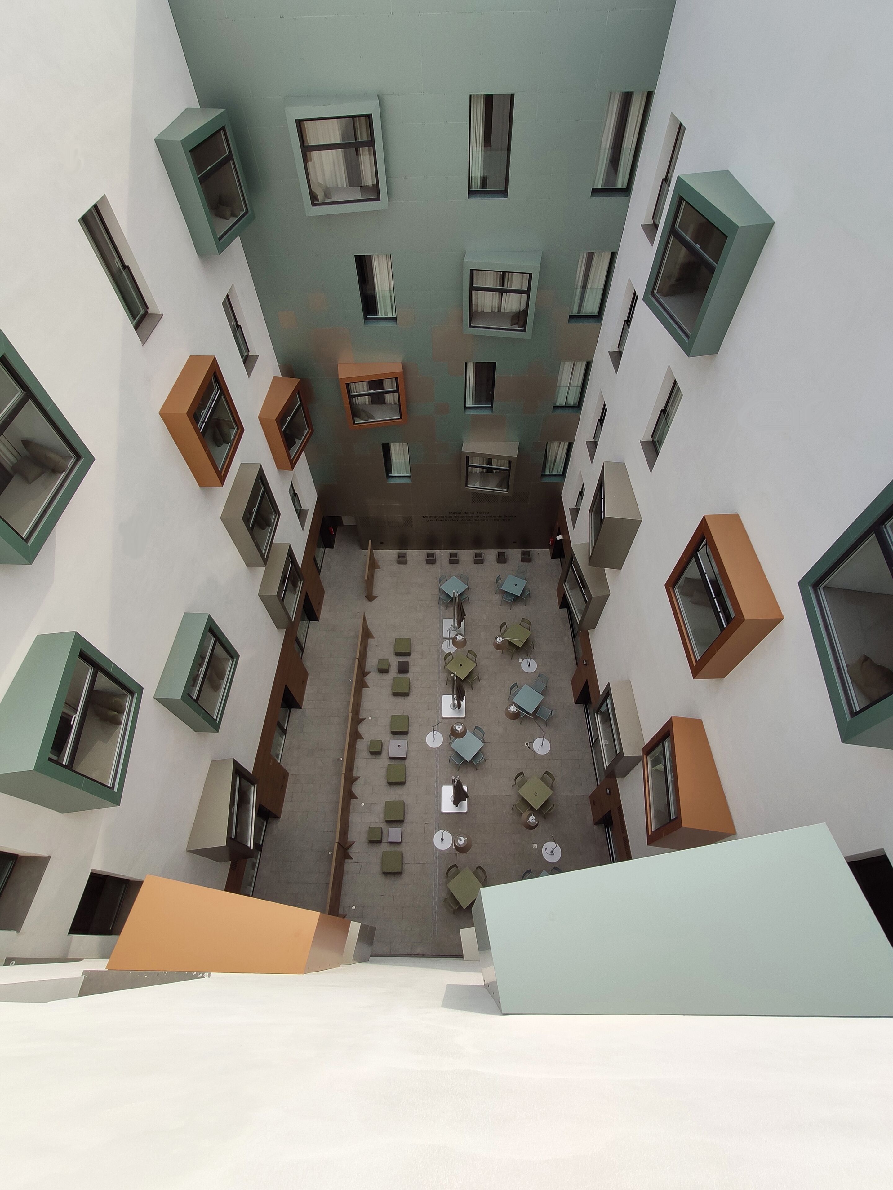 Une cour dotée de nombreuses tables et chaises, entourée d’immeubles avec des fenêtres et des balcons.