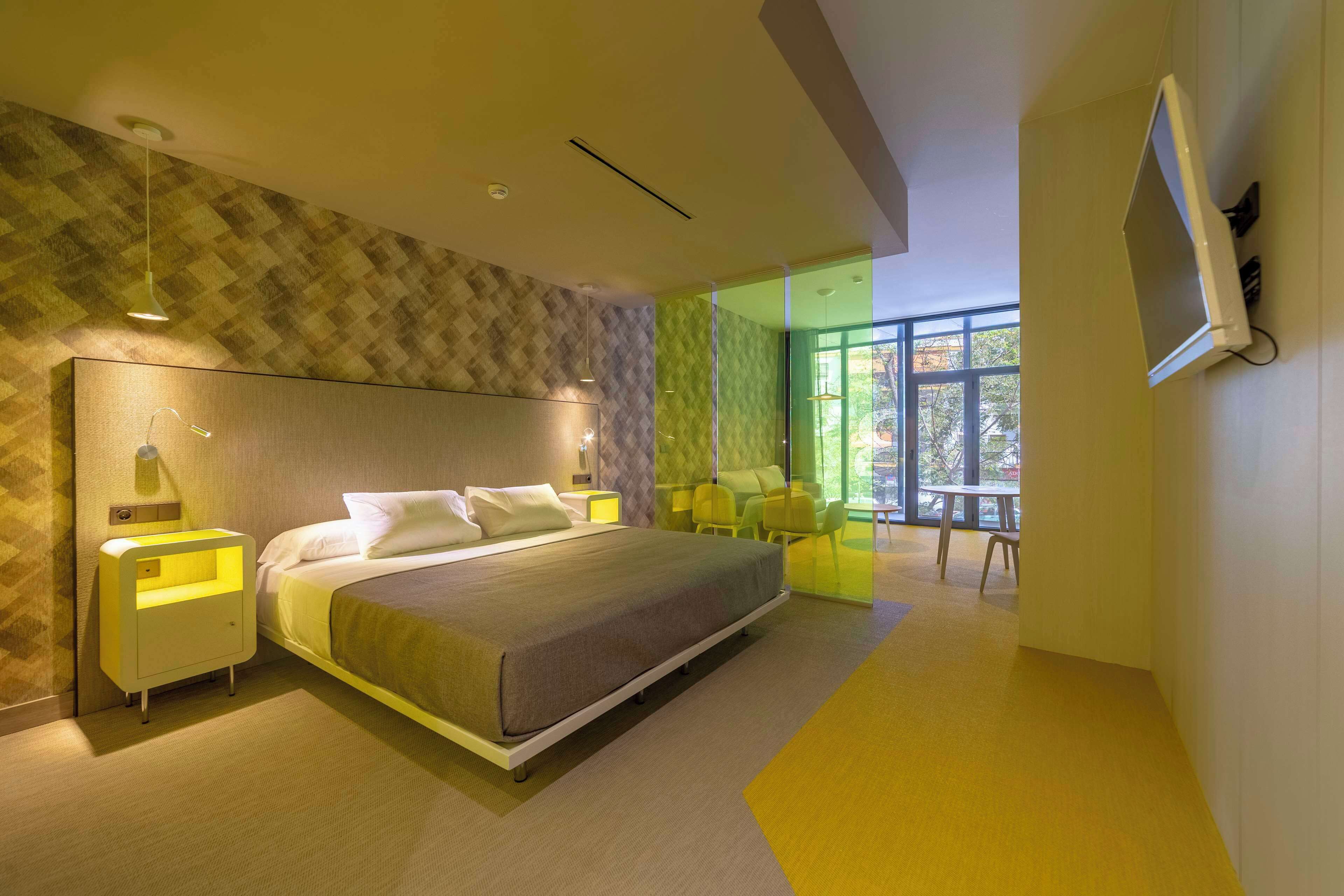 Habitación de hotel moderna con una cama grande, mesitas de noche, un televisor y vistas al exterior.