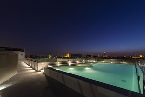 Una piscina en la azotea con vista a un paisaje urbano al atardecer.