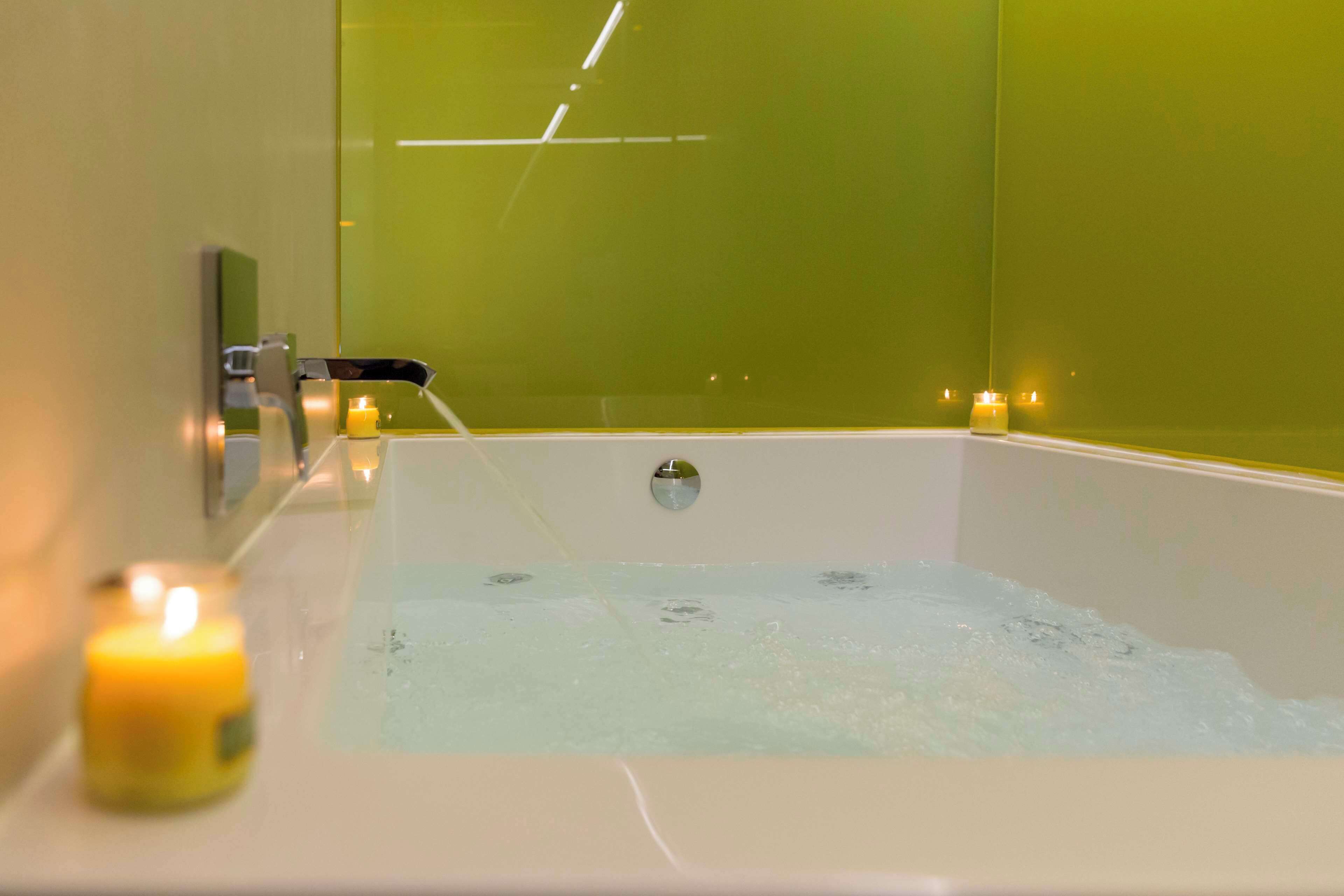 A bathtub with running water, a small candle, and a mirror on the wall.