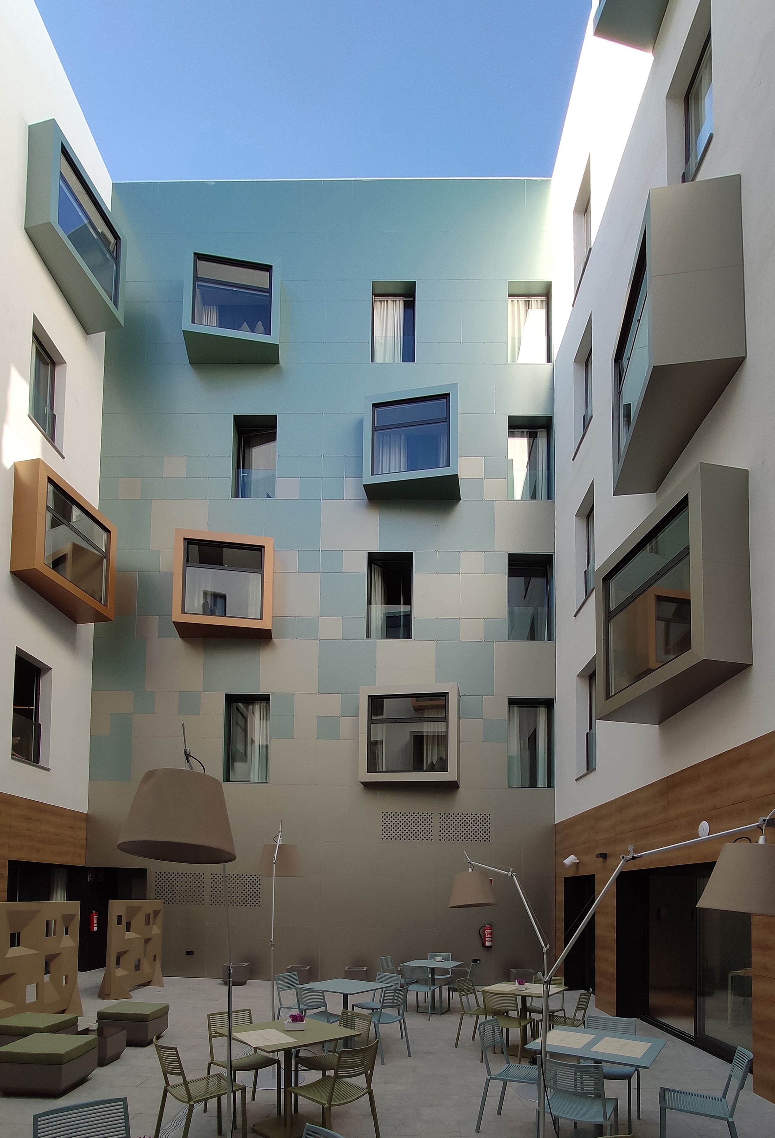 Een modern gebouw met meerdere balkons, buiten zitplaatsen en een heldere lucht.