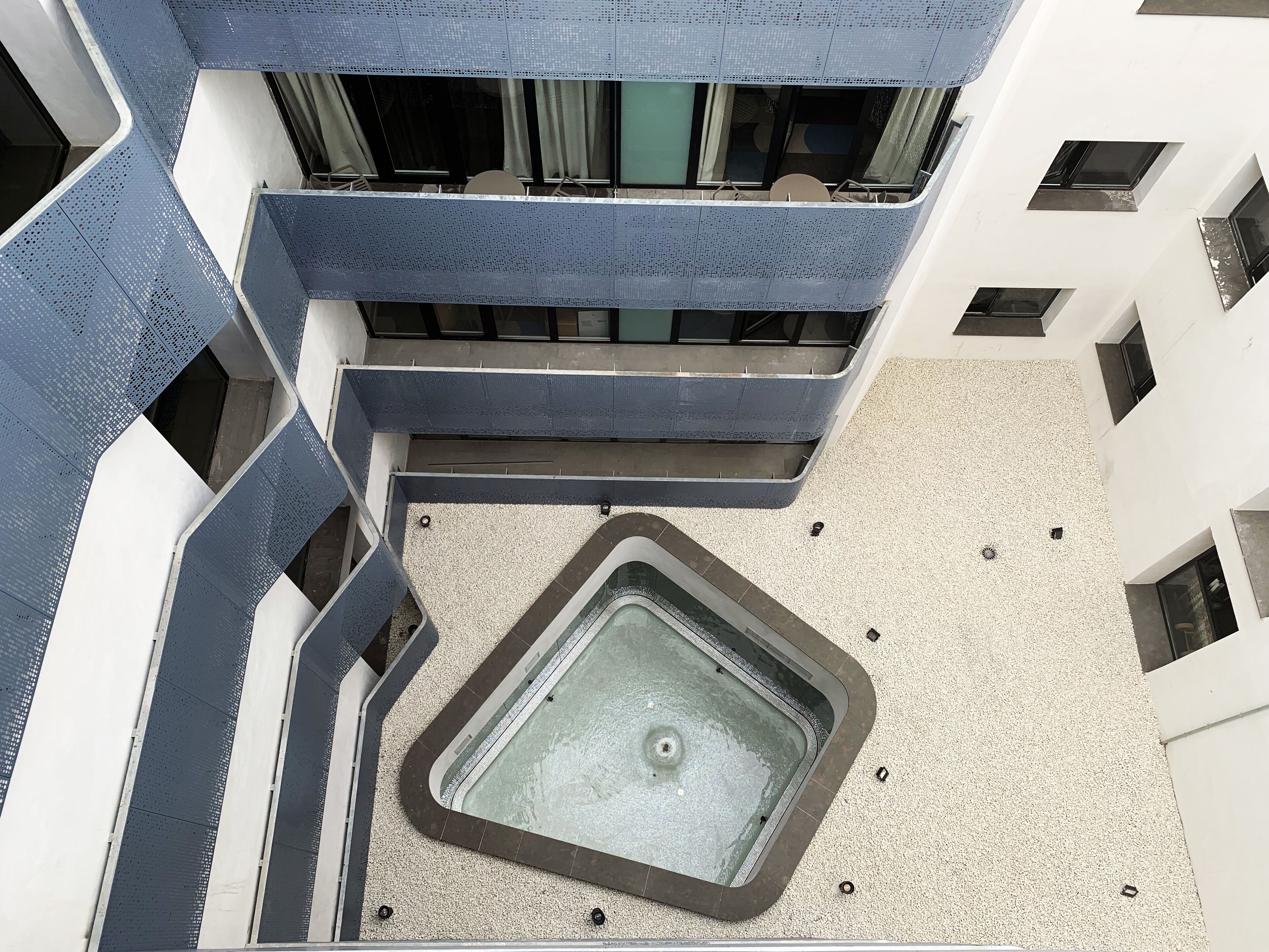 A modern building with a central courtyard featuring a square water feature and a seating area with tables and chairs.