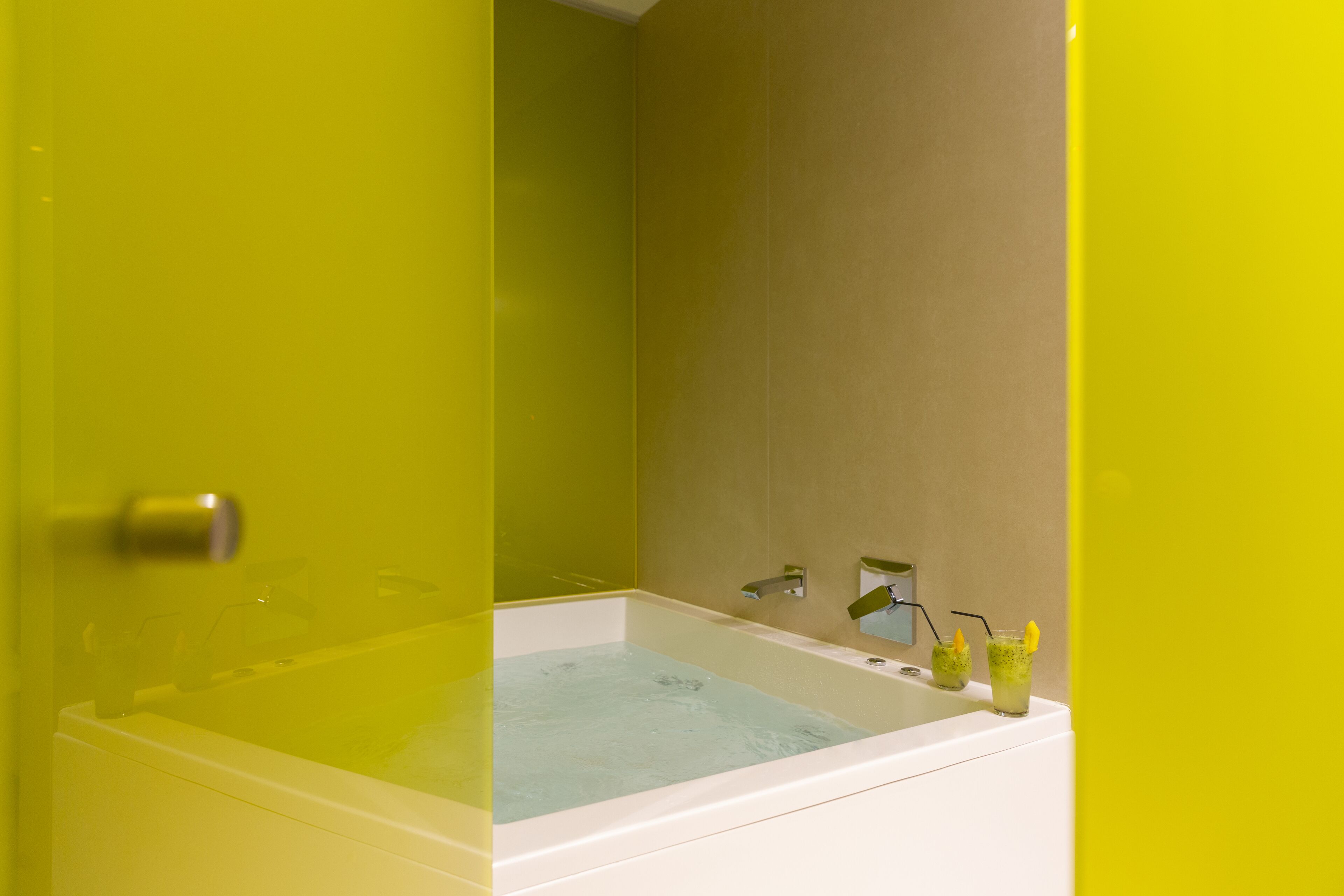 Un baño con bañera, lavamanos y dos vasos de agua sobre el lavamanos.
