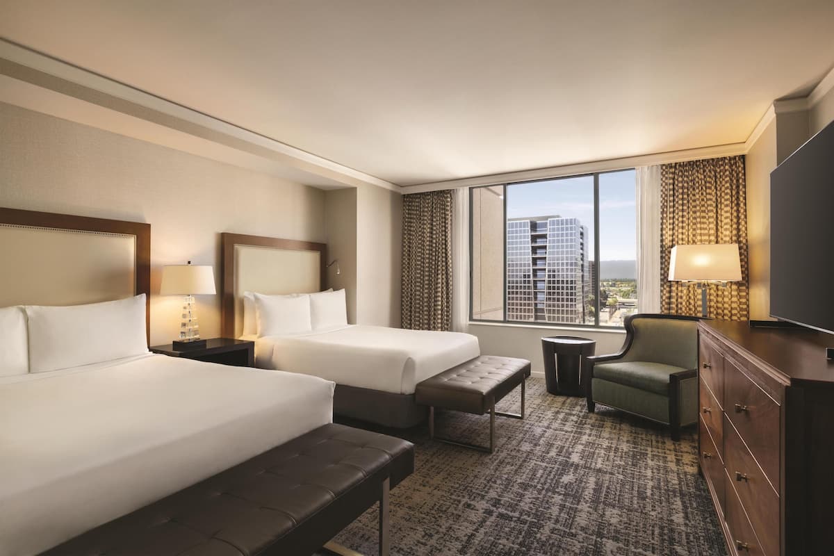 A hotel room with two beds, a sofa, a chair, a TV, a small table, and a window with a city view.
