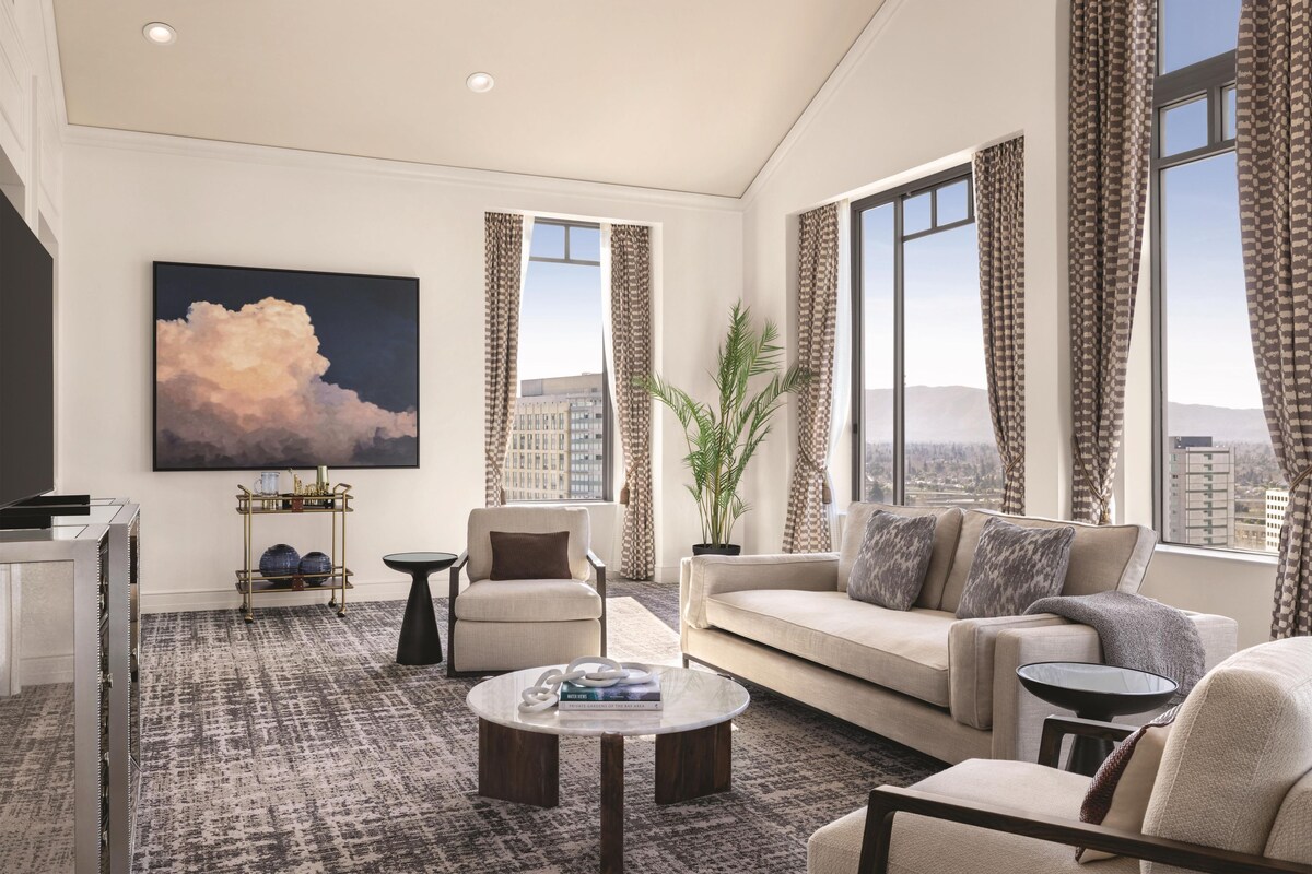 A modern living room with a sofa, armchairs, a coffee table, and a large painting.