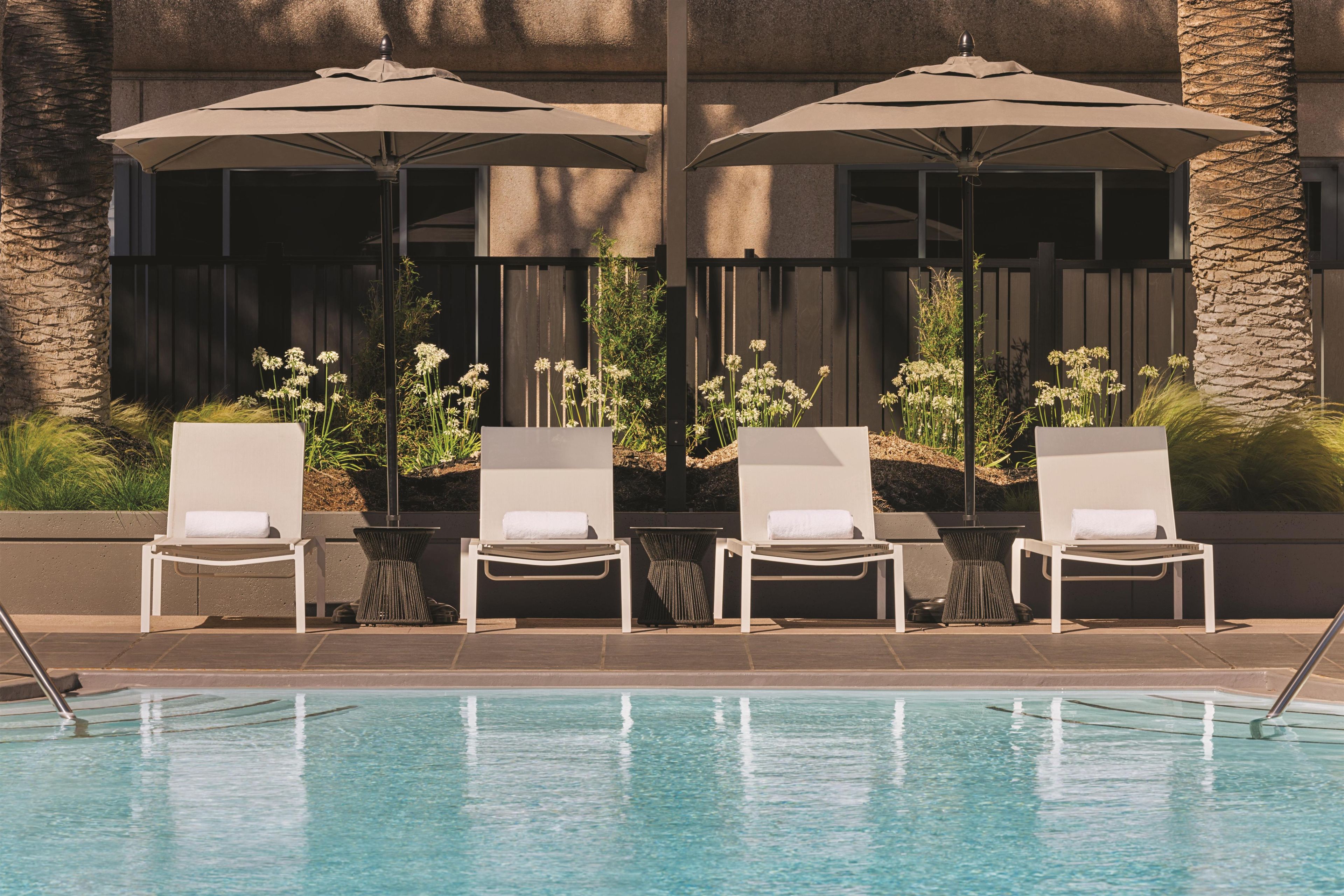 A poolside area with lounge chairs and umbrellas, a pool, and a building with a stone facade.