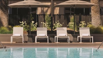 A poolside area with lounge chairs and umbrellas, a pool, and a building with a stone facade.