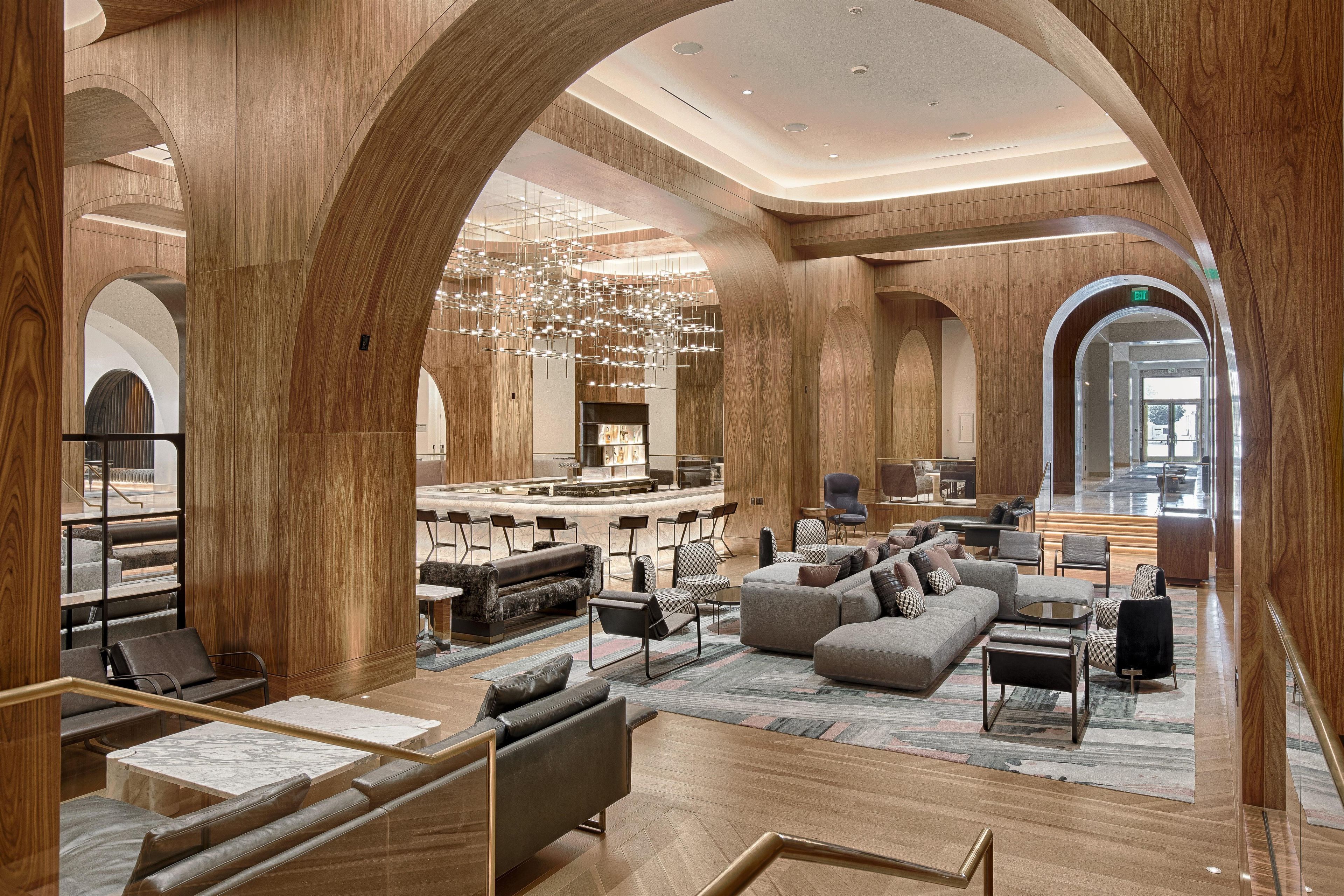 A spacious lobby with high wooden arches, a central seating area with sofas and chairs, and a bar with stools.
