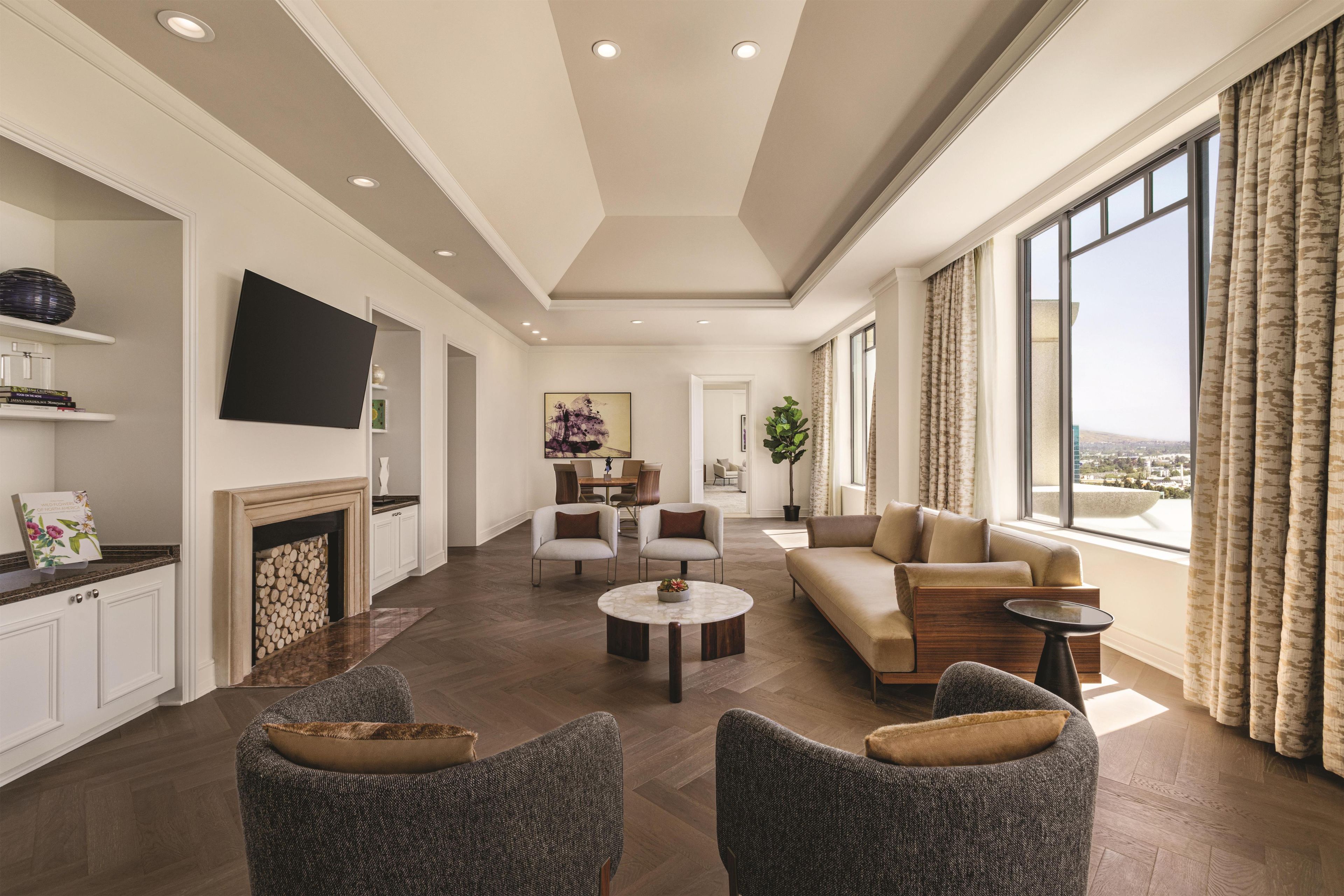 A modern living room with a fireplace, a sofa, a TV, and a large window with curtains.