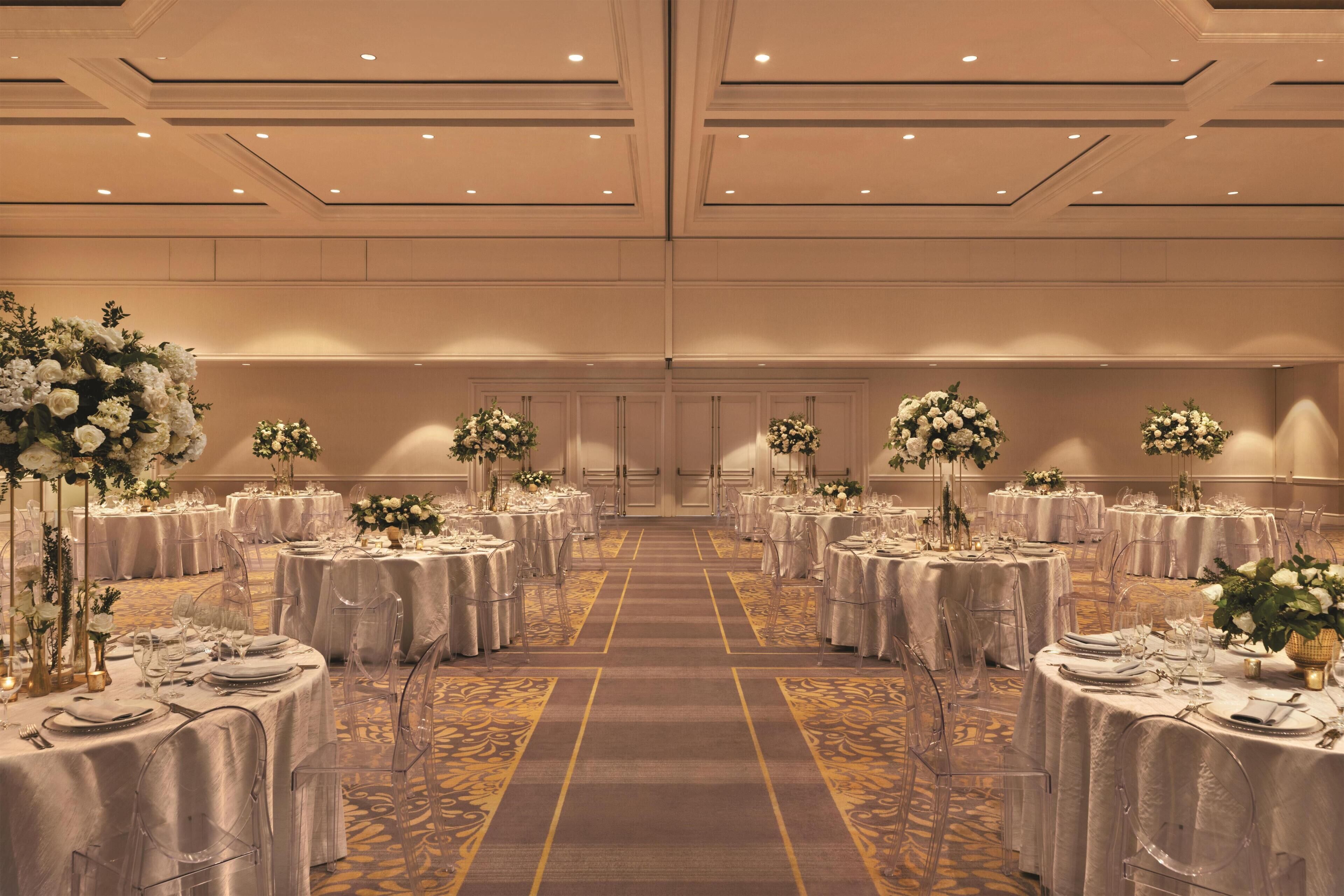 Ein Festsaal mit runden Tischen, klaren Stühlen und floralen Mittelpunkten.