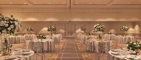 Ein Festsaal mit runden Tischen, klaren Stühlen und floralen Mittelpunkten.