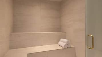 A modern bathroom with a shower area, a bench with towels, and a glass door with a gold handle.