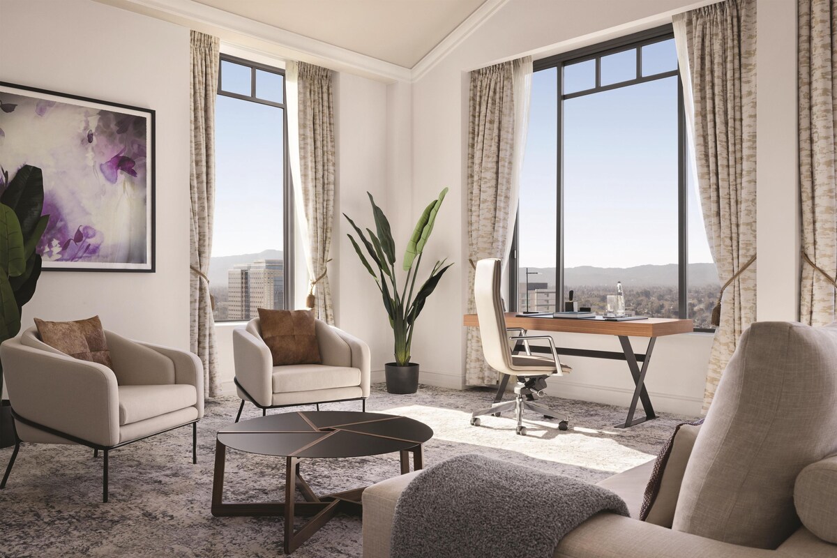 A modern living room with a large window, a potted plant, and a desk with a chair.