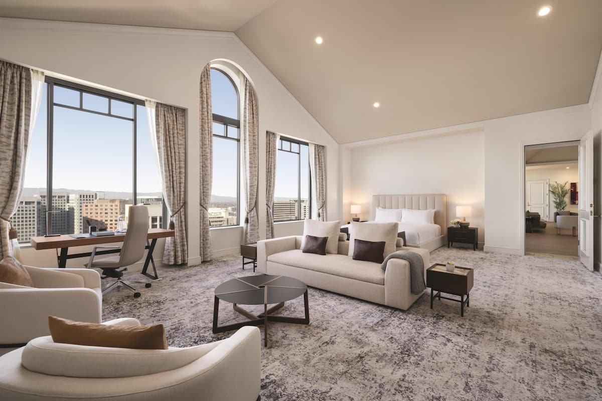 A spacious living room with a high ceiling, large windows, a sofa, a coffee table, and a desk.
