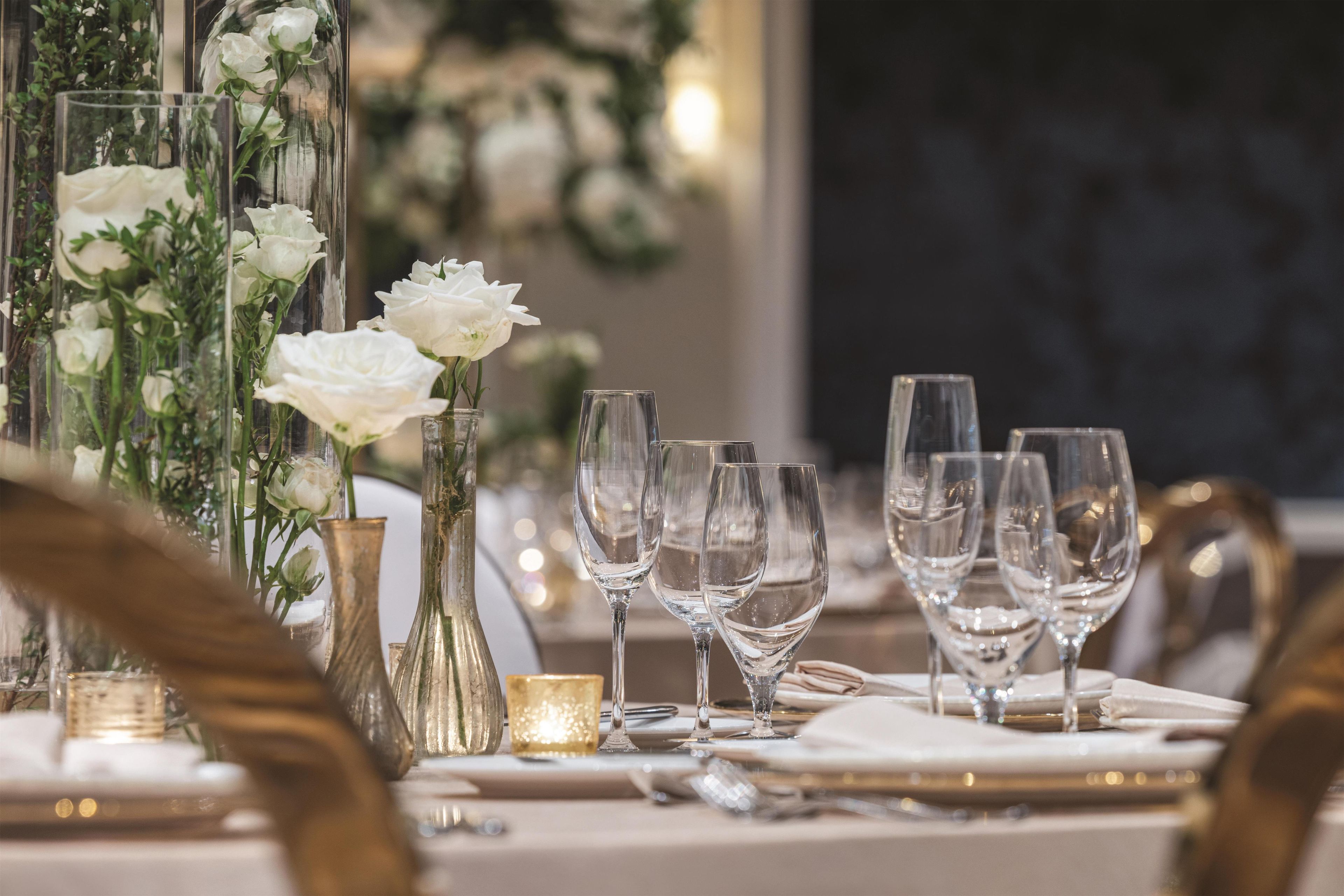 A table set with clear glassware, white roses in a vase, and a candle.
