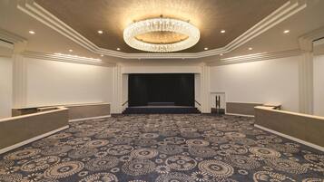 A spacious hotel lobby with a patterned carpet, a grand chandelier, and a stage at the far end.