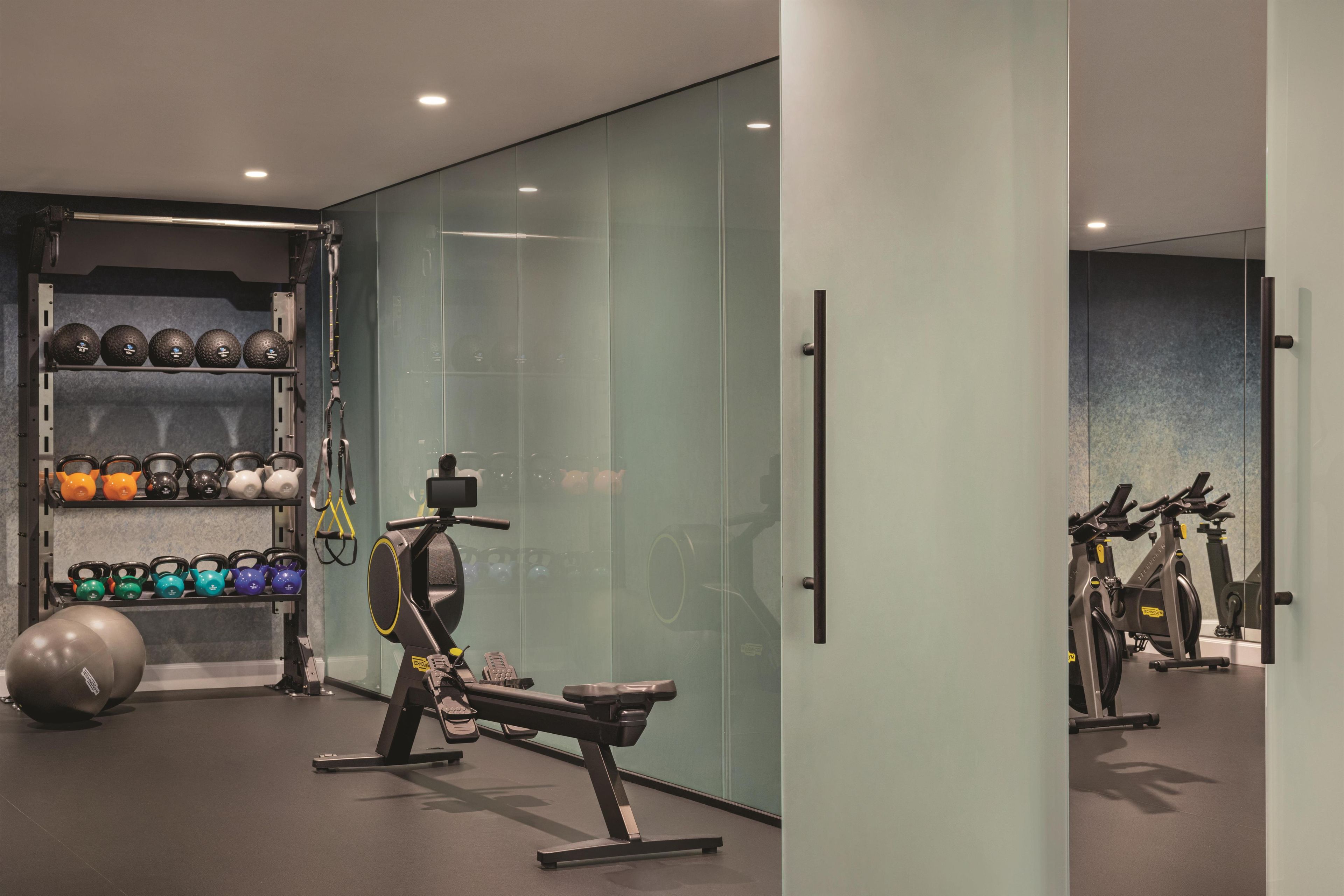 A modern gym with exercise equipment, a weight rack, and a mirrored wall.