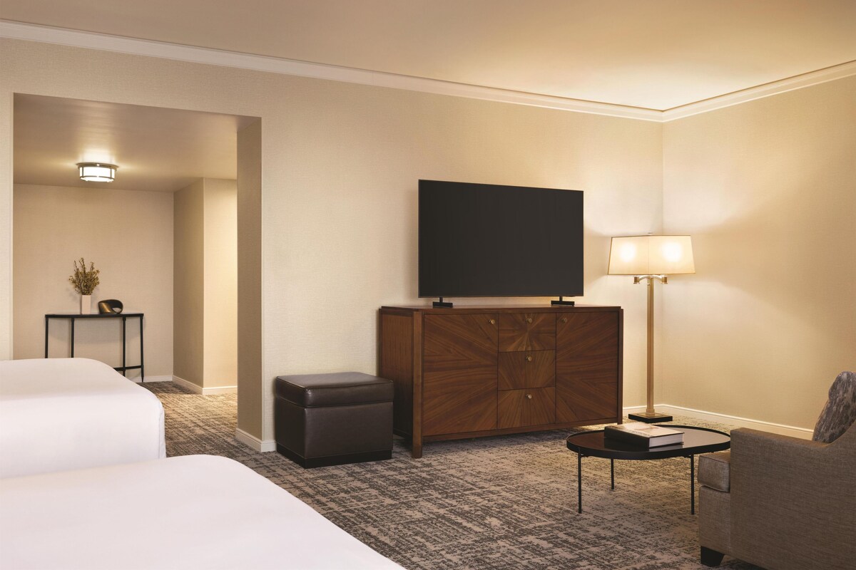 A hotel room with a bed, a sofa, a small table, a TV, a cabinet, and a lamp.