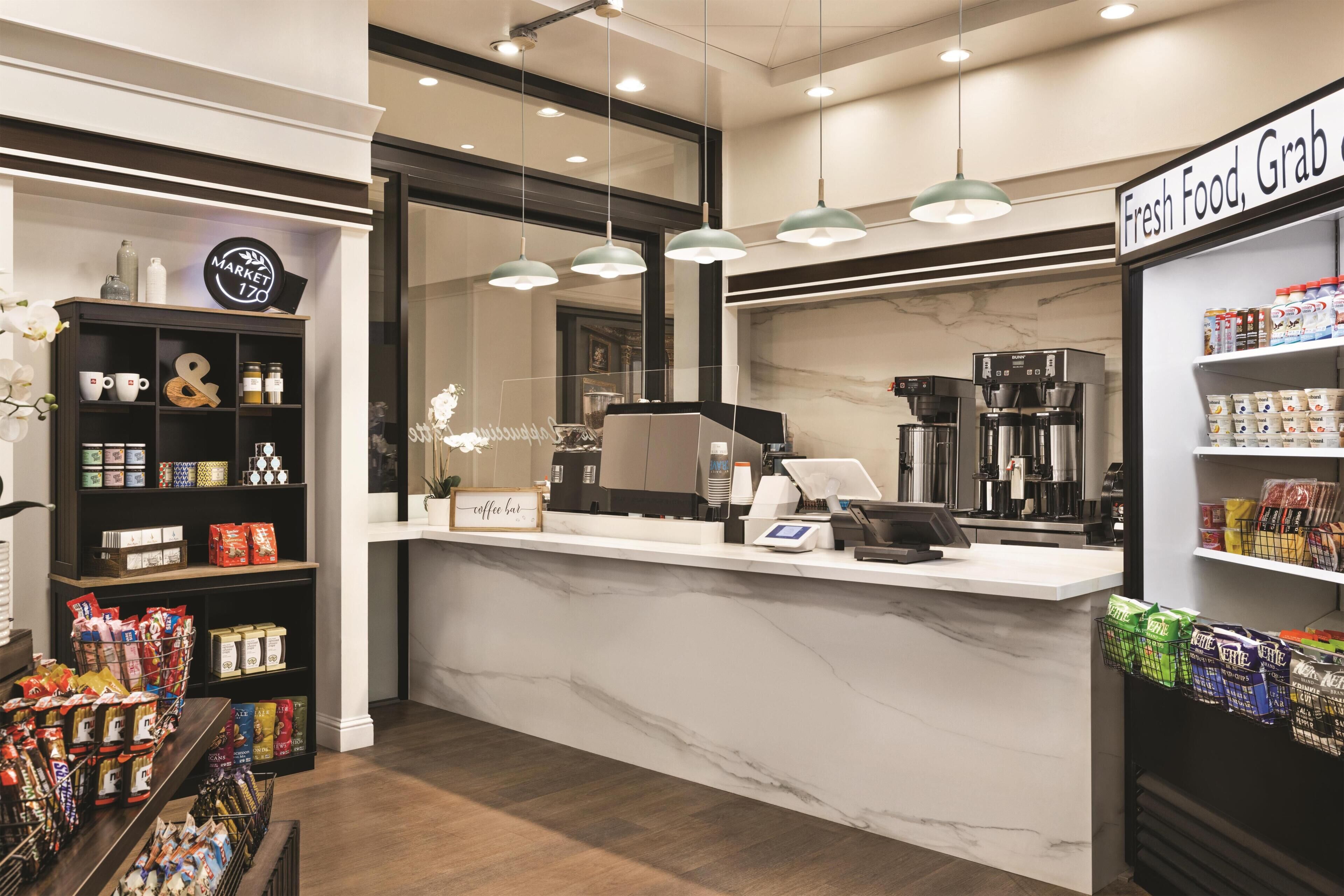 Un interno di caffetteria con un bancone in marmo, macchine per caffè e scaffali pieni di caffè in grani e snack.