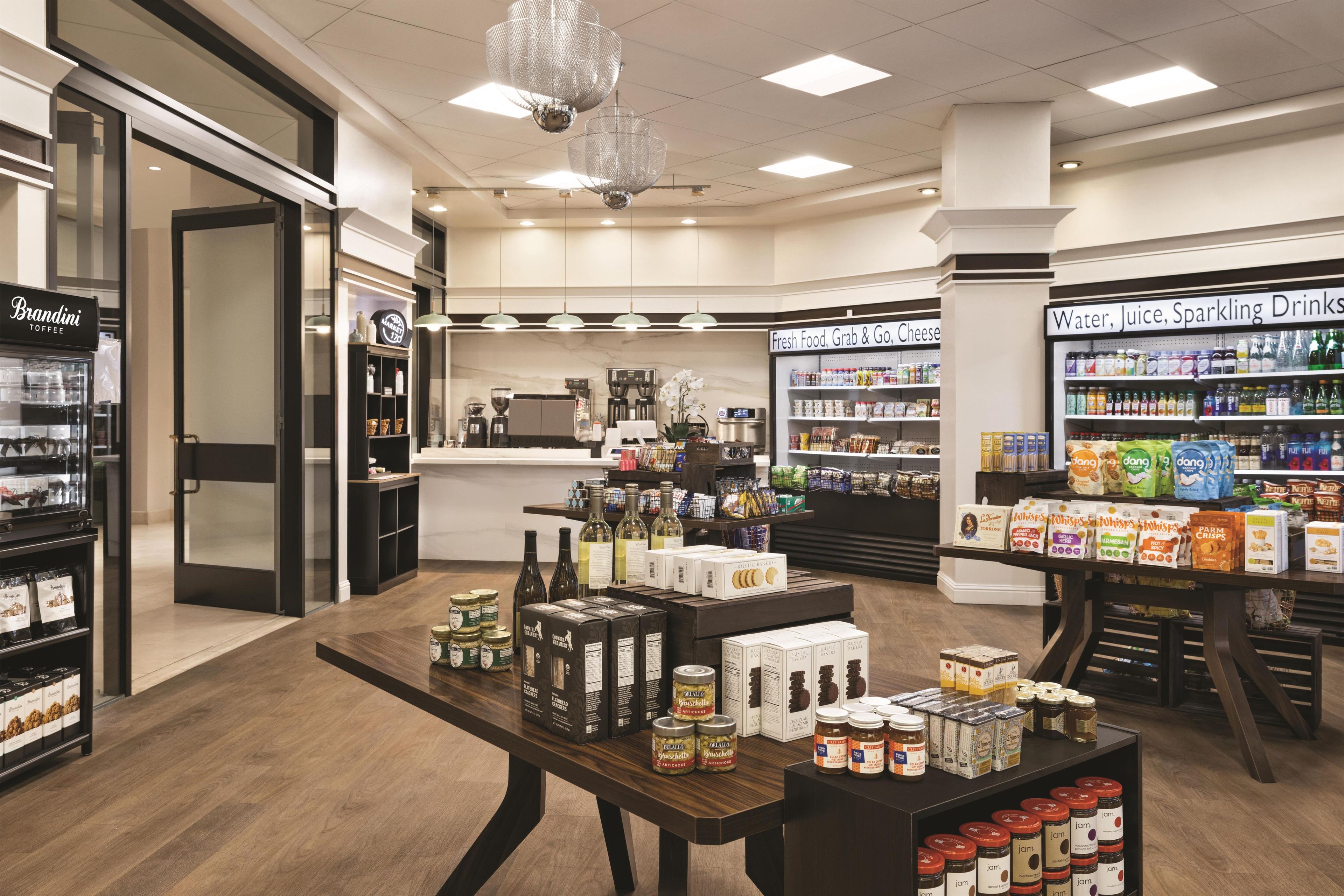 Interior de una tienda de comestibles con estantes llenos de diversos productos alimenticios, una estación de café y una sección refrigerada para productos lácteos.