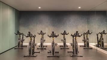 Ein Fitnessraum mit in Reihen angeordneten Ergometer, einer großen Spiegelwand und einer schlichten Decke mit eingelassener Beleuchtung.