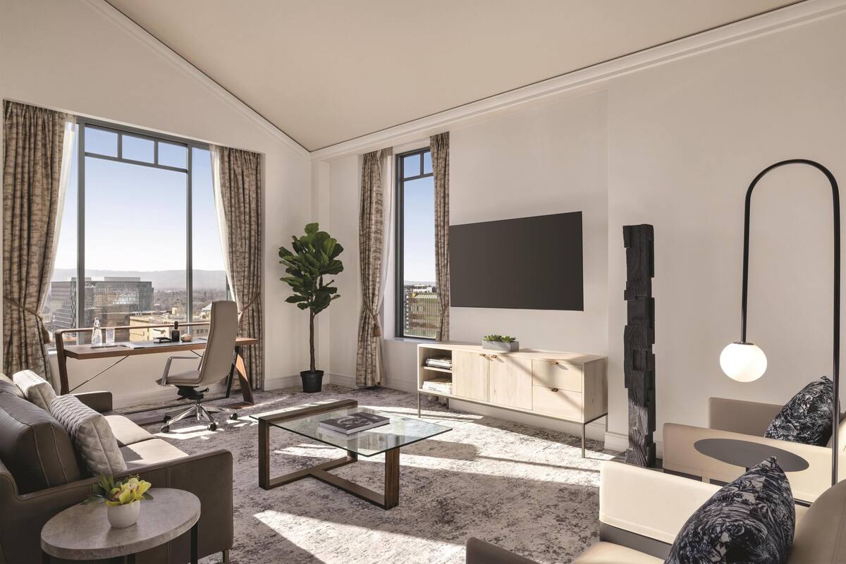 A modern living room with a sofa, coffee table, and a desk with a chair. There is a large window with curtains, a potted plant, and a flat-screen TV mounted on the wall.