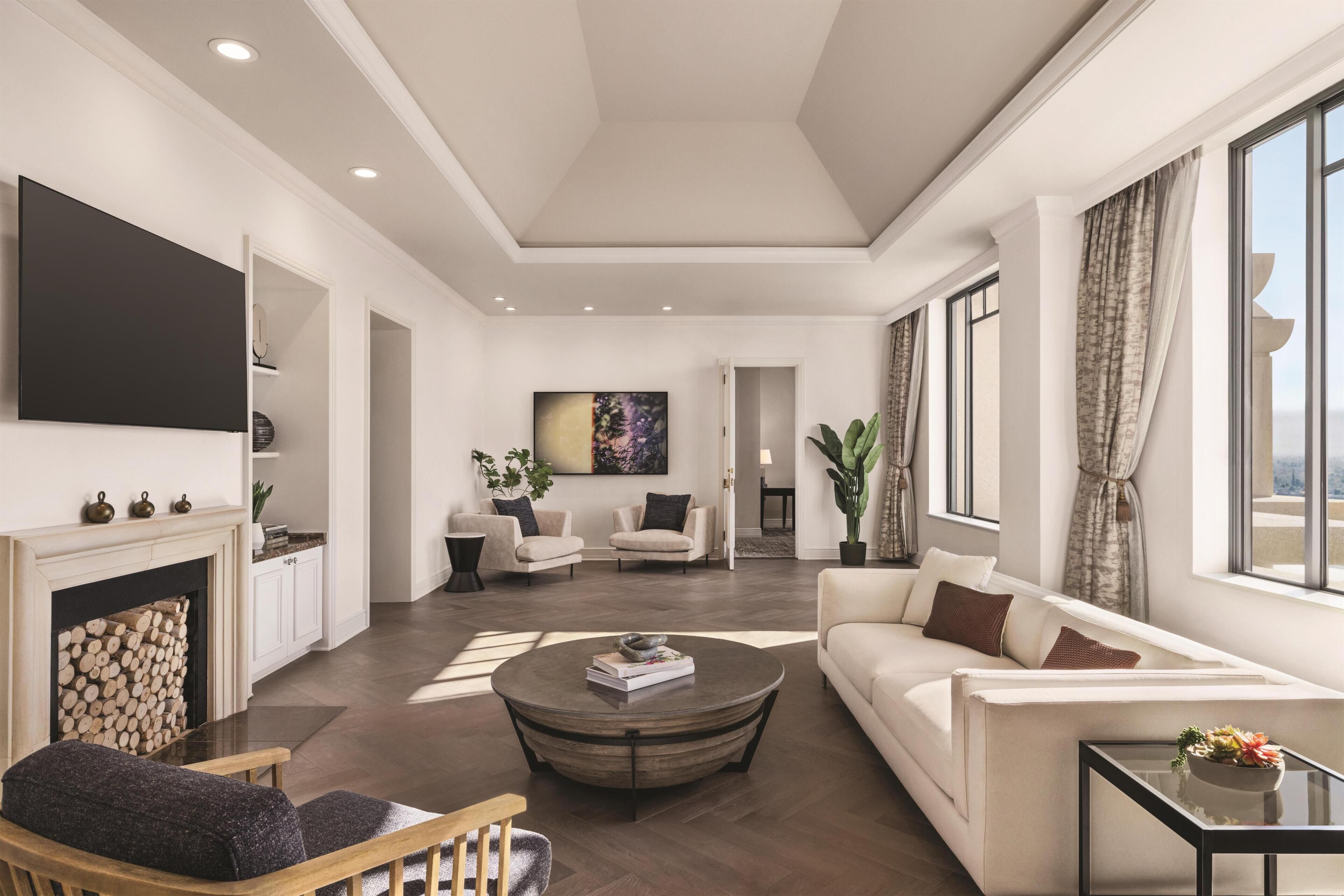 A modern living room with a fireplace, a round coffee table, sofas, and a large window with curtains.