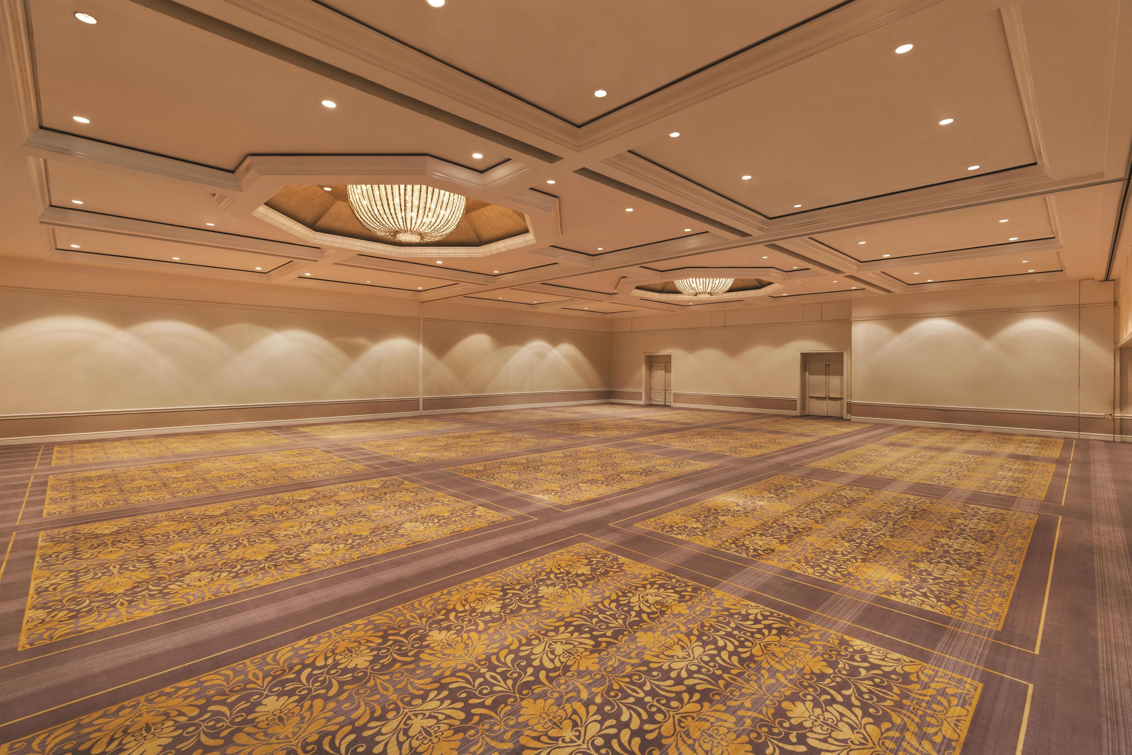 A large, empty conference room with patterned carpet, recessed lighting, and a central chandelier.