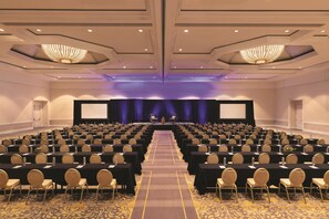 A conference room with rows of tables and chairs, a stage with a screen, and chandeliers. - Signia by Hilton San Jose (San Jose)