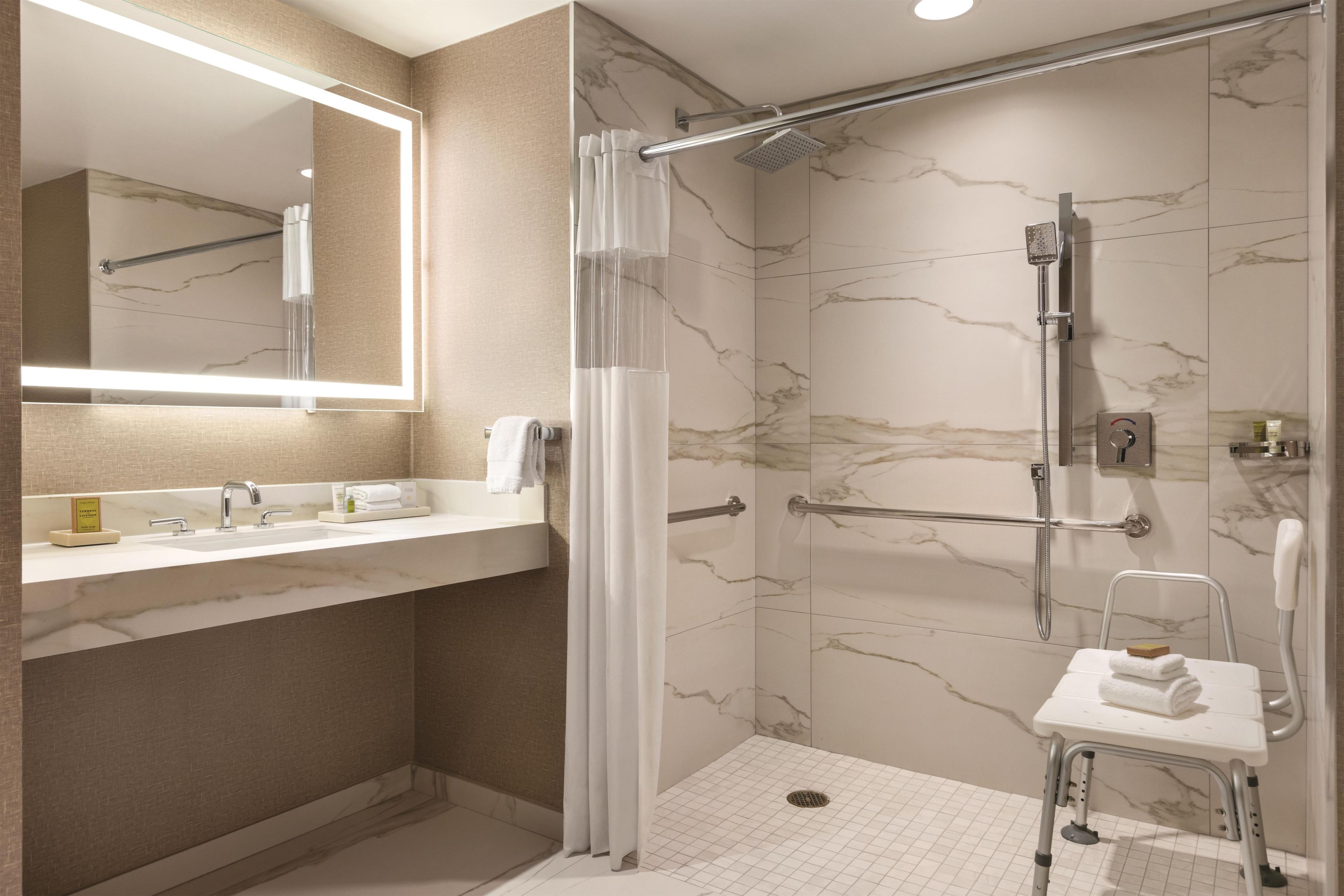 Une salle de bain moderne équipée d’une douche, d’un meuble-lavabo avec miroir et d’un tabouret accessible aux personnes en fauteuil roulant.