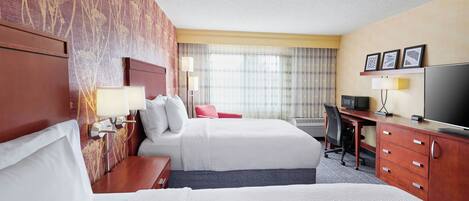 A hotel room with two beds, a desk, a television, and a window with curtains.