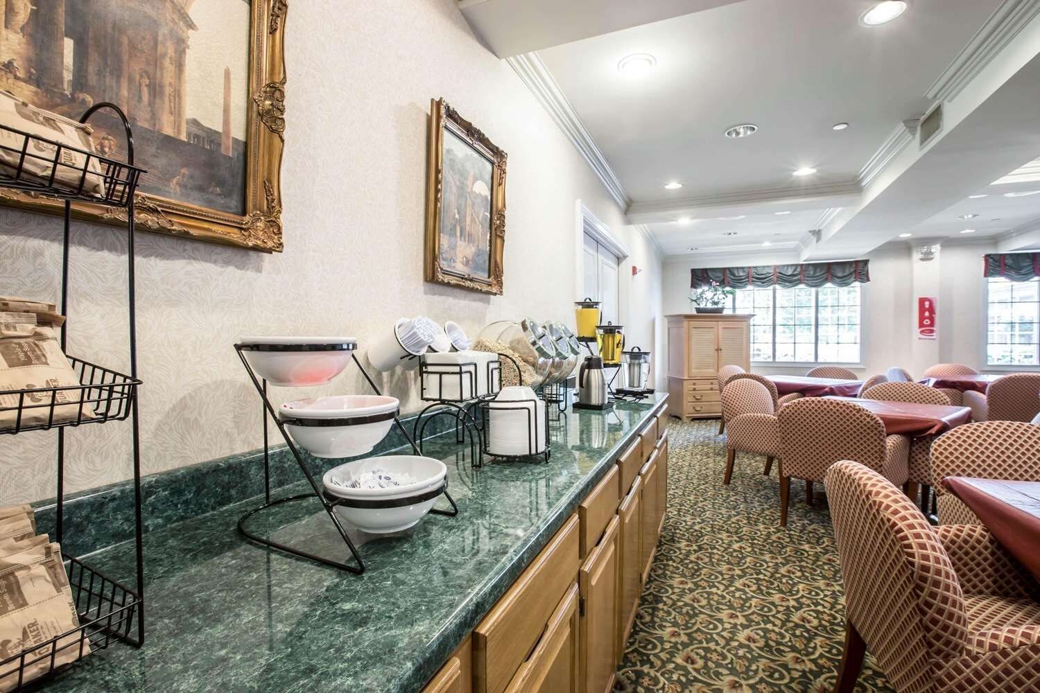 A hotel dining area with a marble counter, dining tables, chairs, and a patterned carpet.